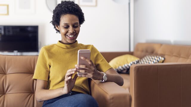 Smiling young woman at home using smartphone SMALL
